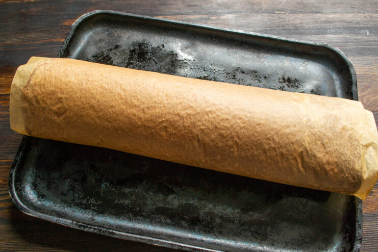Bizcocho de chocolate enrollado en caliente junto con su papel vegetal de horneado.