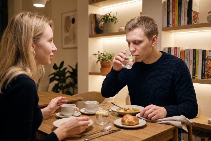 Hombre bebiendo agua mientras conversa animadamente con una mujer durante una cena en una cafetería acogedora.