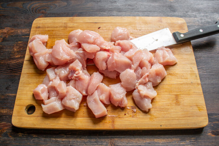 Pechuga de pollo cortada en dados sobre una tabla de cortar de madera