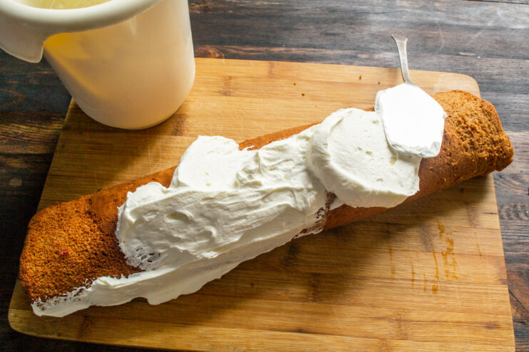 Brazo de gitano cubierto de crema blanca extendida de manera uniforme por toda la superficie.