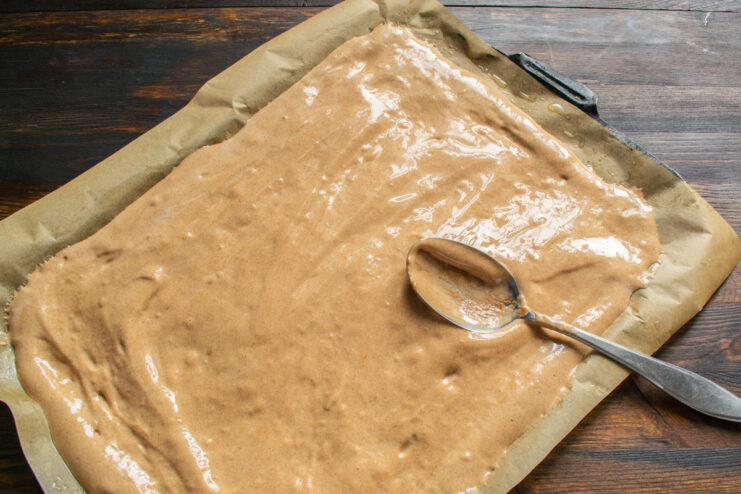 Masa de chocolate extendida finamente sobre una bandeja de horno forrada con papel vegetal.