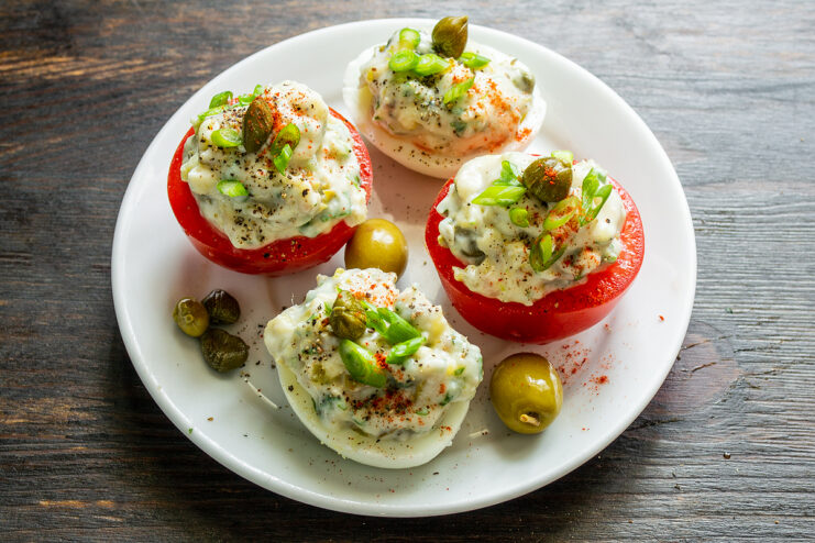 Huevos y tomates rellenos decorados con alcaparras y cebolleta
