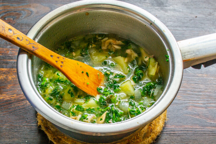 Trozos de pollo cocido desmenuzado añadiéndose a la olla con la sopa de ortigas