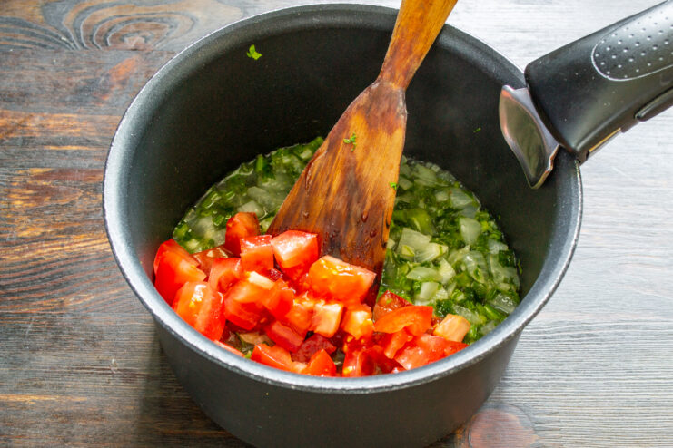 Incorporación del tomate fresco Añadiendo dados de tomate fresco al sofrito de verduras en la cazuela.