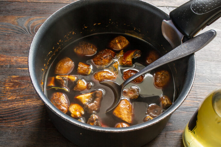 Vertiendo vinagre sobre el caldo caliente de los champiñones en la olla