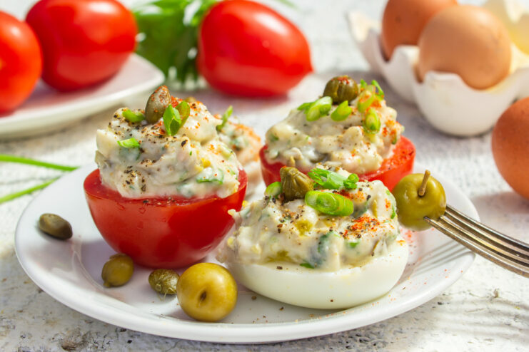 Huevos y tomates rellenos con anchoas servidos en un plato llano