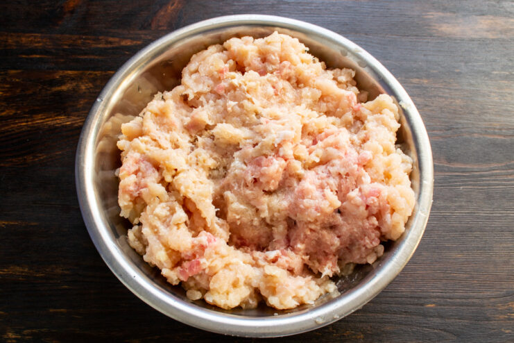Carne picada cruda de pollo y cerdo mezclada en un recipiente metálico