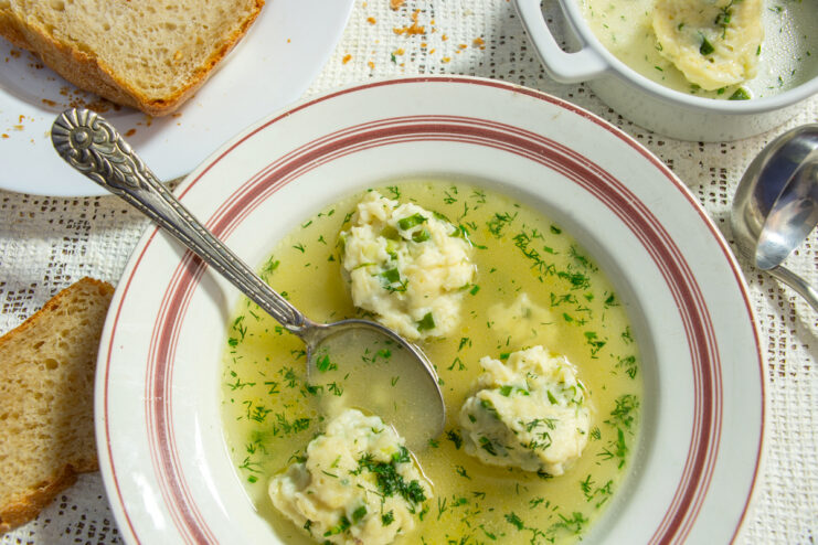 Caldo de pollo transparente con quenelles de arroz, hierbas frescas y pan en un plato hondo