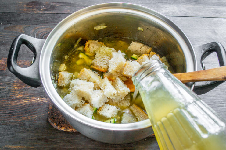 Vertiendo caldo de pollo en una olla con verduras y trozos de pan.