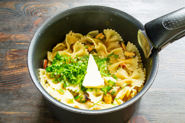 Toque final con mantequilla Añadiendo una nuez de mantequilla a la cazuela con farfalle y mejillones.
