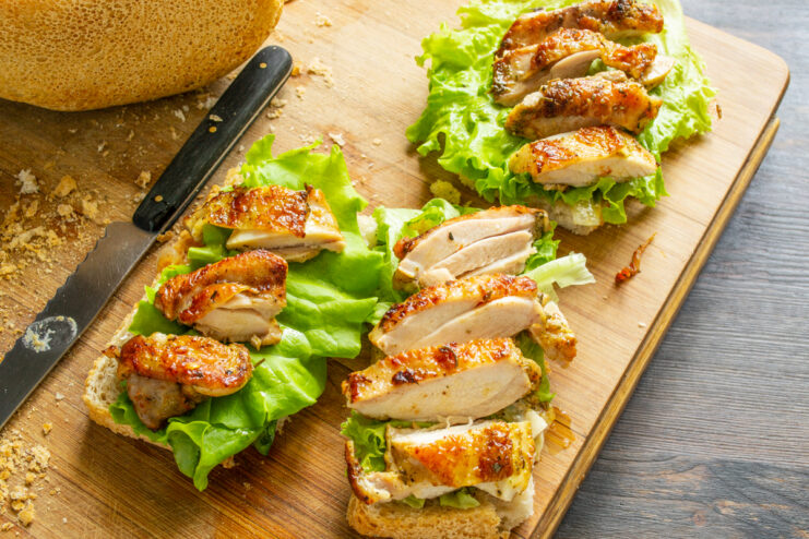Trozos gruesos de pollo dorado colocados sobre las hojas de lechuga en el pan.