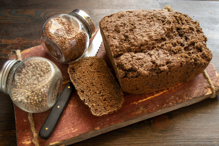 Servir el pan de lino Rebanada de pan de lino en una tabla junto a unos tarros de especias
