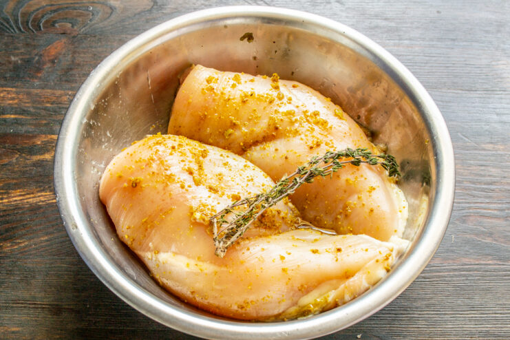 Proceso de marinado de pechuga de pollo con especias y tomillo fresco dentro de un bol