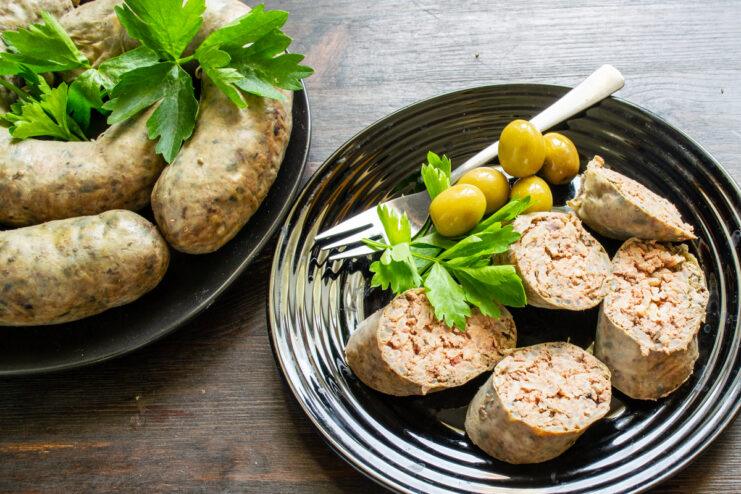 Rodajas de embutido de hígado servidas en un plato negro con aceitunas.