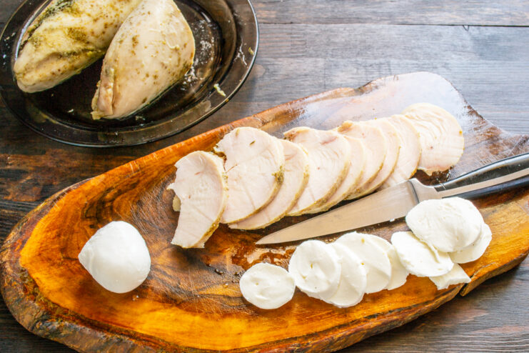Rodajas de mozzarella y pollo cortado en lonchas sobre una tabla de cocina de madera