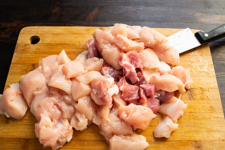 Trozos de pechuga de pollo y carne de cerdo en dados sobre una tabla