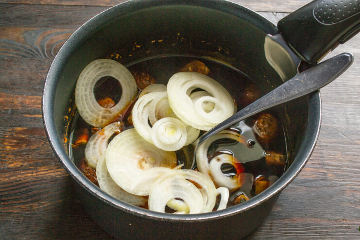 Aros de cebolla cruda cayendo sobre el guiso caliente de champiñones