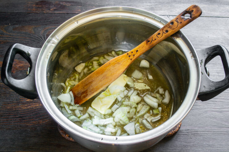 Cebolla picada pochándose con mantequilla y caldo en una olla de acero inoxidable.