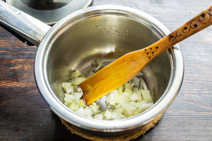 Cebolla picada dorándose en una olla con aceite caliente a fuego medio