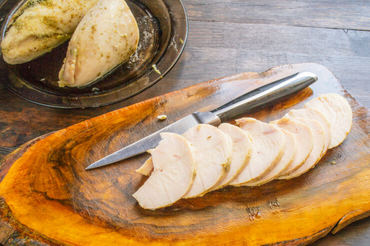 Corte de pechuga de pollo jugosa en lonchas finas sobre una tabla de madera