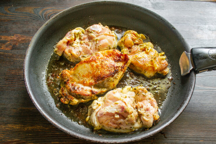 Muslos de pollo dorándose en una sartén caliente a fuego fuerte.