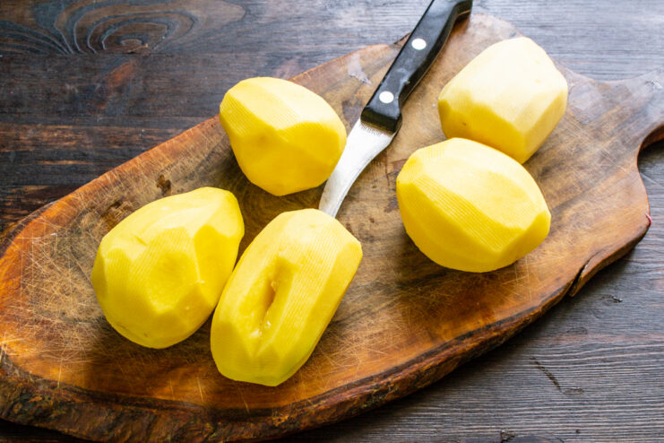 Patatas crudas peladas sobre una tabla de cortar de madera