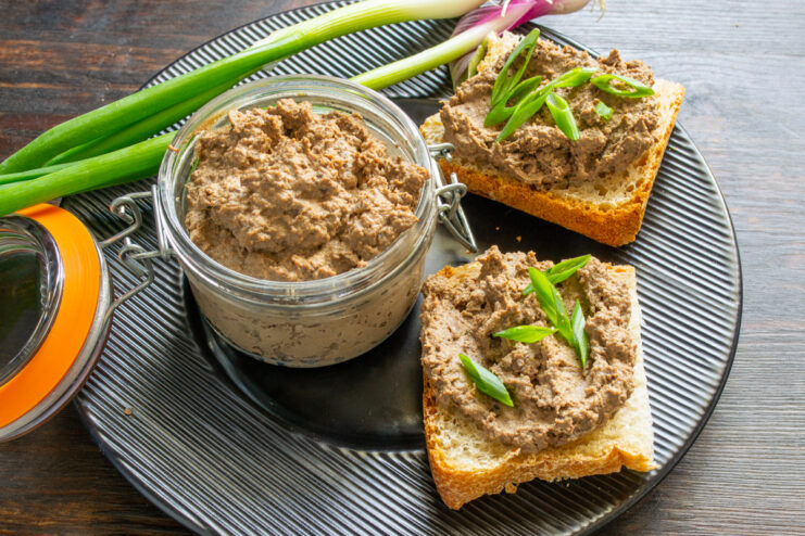 Presentación del paté Paté en tarro de cristal junto a rebanadas de pan untadas en plato negro