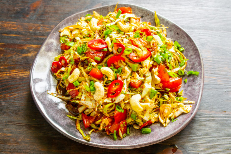Ensalada de col con tomate y anacardos servida en un plato llano.