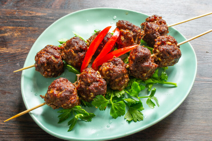Brochetas de albóndigas decoradas con pimiento rojo y hierbas