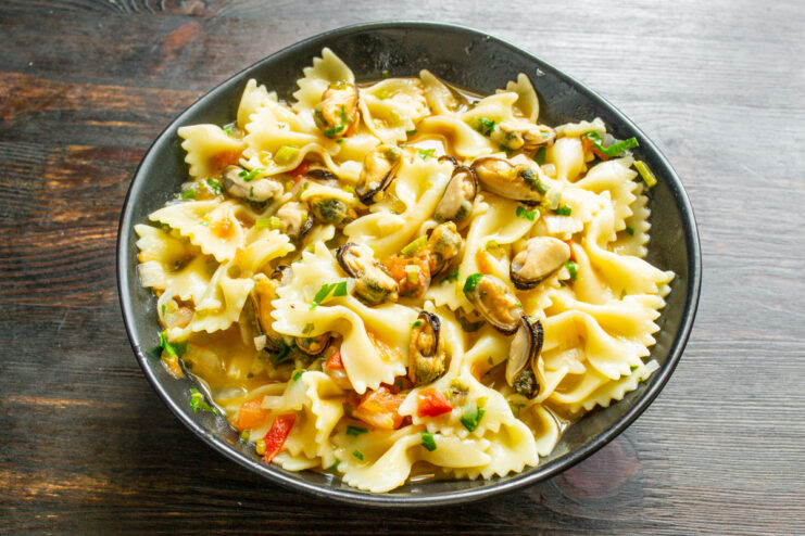 Emplatado de los farfalle con mejillones Ración de farfalle con mejillones recién servida en un plato hondo oscuro con queso rallado.