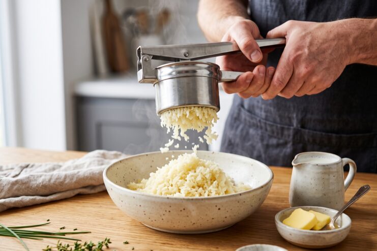 Proceso para elaborar puré prensando la patata con una herramienta manual sobre un bol profundo.