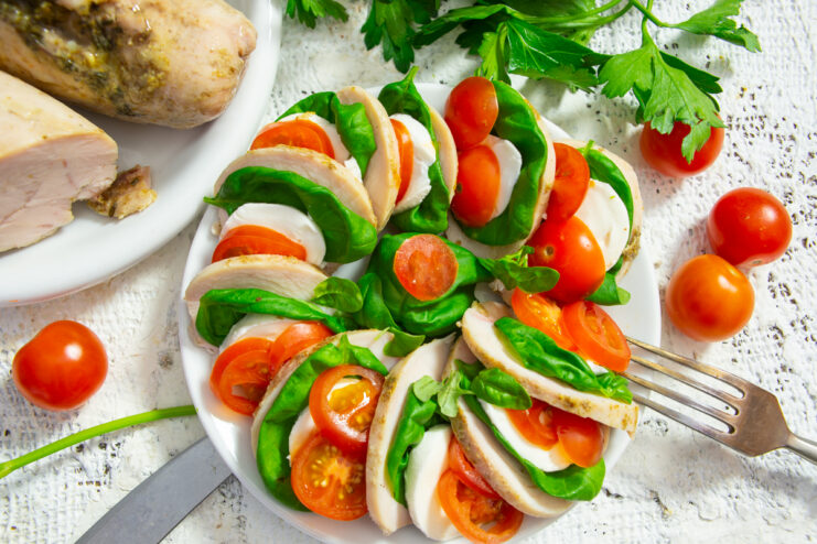 Ensalada caprese con pechuga de pollo, rodajas de mozzarella, tomates y hojas de albahaca fresca