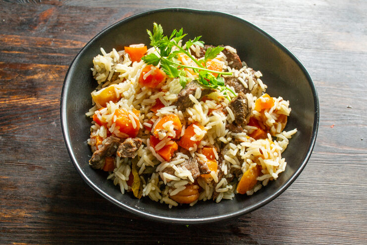Servicio del plov en un plato hondo con carne y orejones arriba