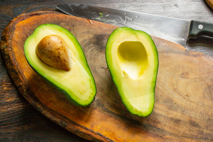 Preparar el aguacate para la salsa Aguacate maduro cortado por la mitad sobre una tabla de madera