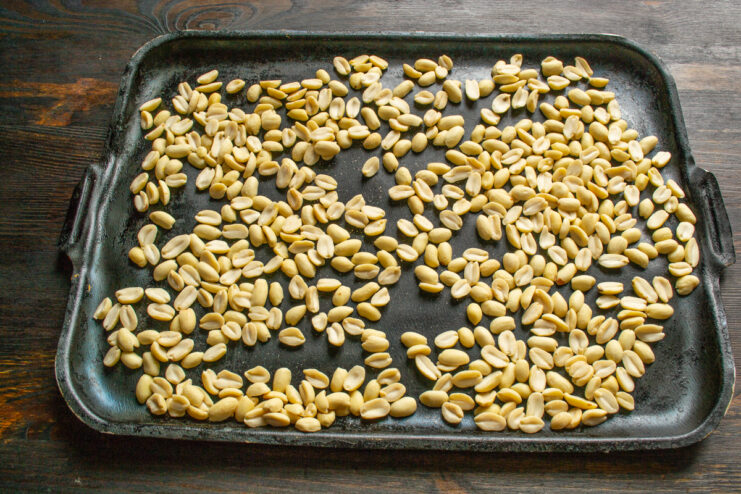 Preparar los cacahuetes para tostarlos Cacahuetes crudos y pelados extendidos sobre una bandeja de horno.