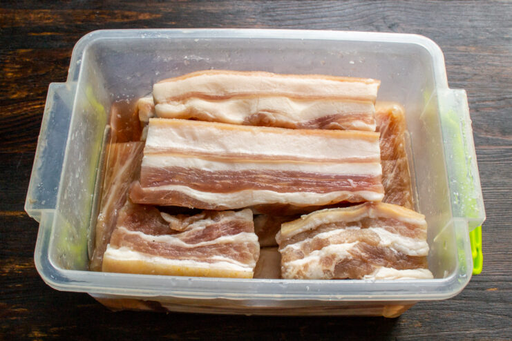 Trozos de panceta de cerdo cubiertos de sal y azúcar en un recipiente