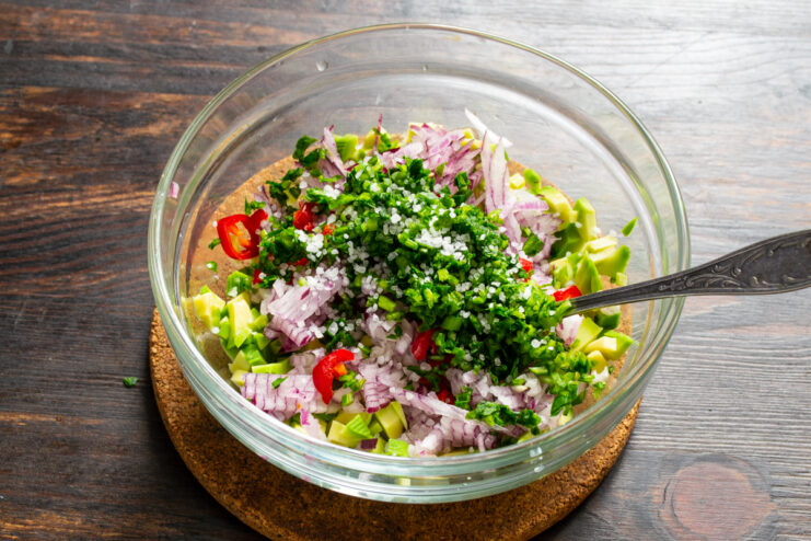 Añadir hierbas frescas y sal Añadiendo cilantro fresco picado y sal marina al bol con aguacate